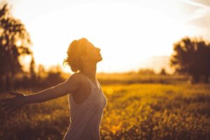 woman alone in a sunny field with arms stretched behind her