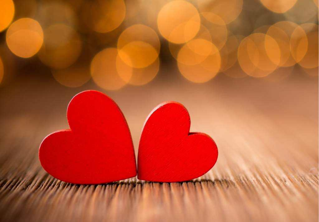 Two red, wooden hearts rested against each other with blurred twinkle lights behind them.