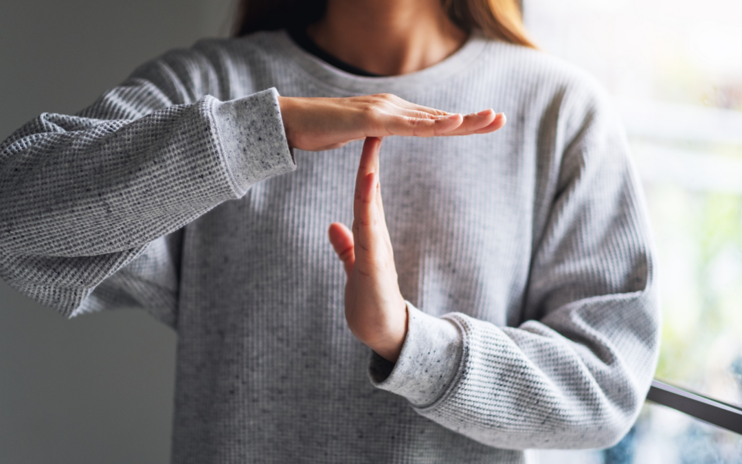 A woman in a grey sweatshirt making a "time out" signal with her hands.