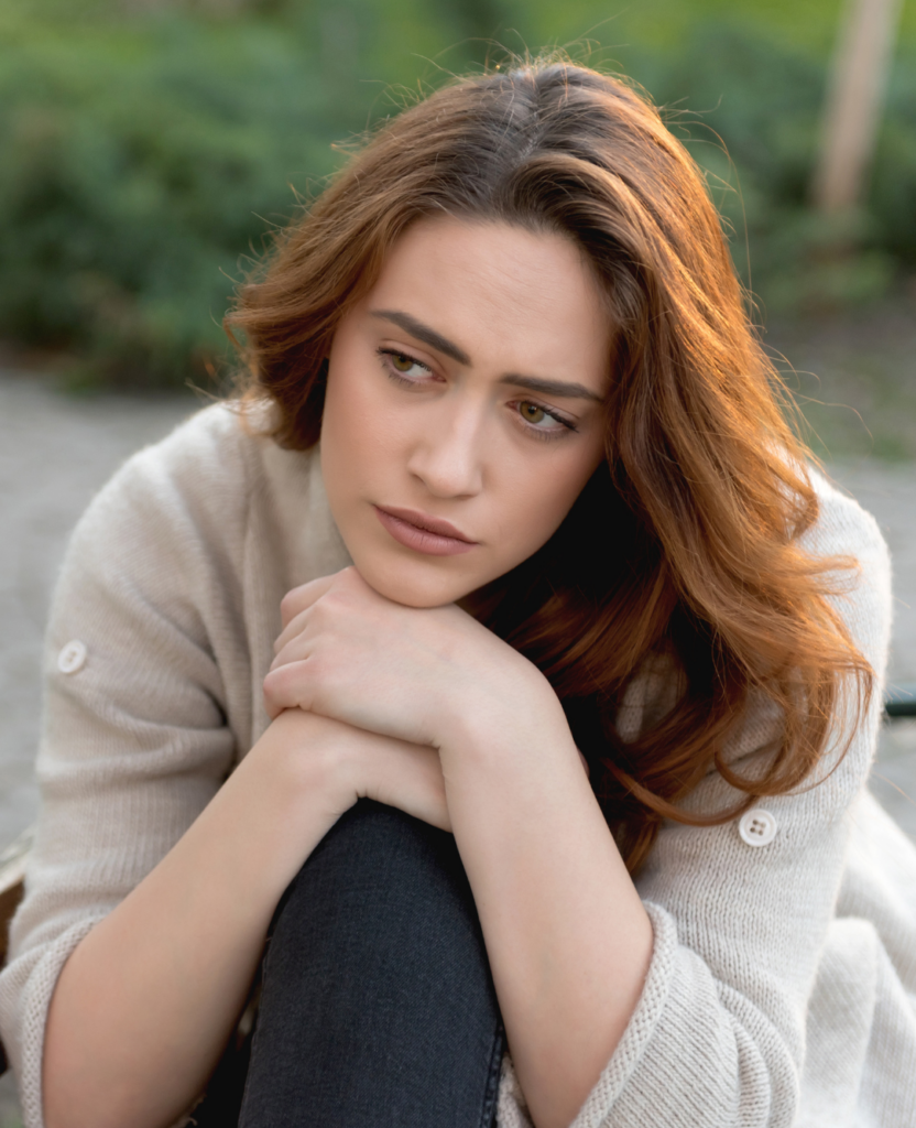 Sad young woman sitting alone on a park bench, looking thoughtful and contemplative.