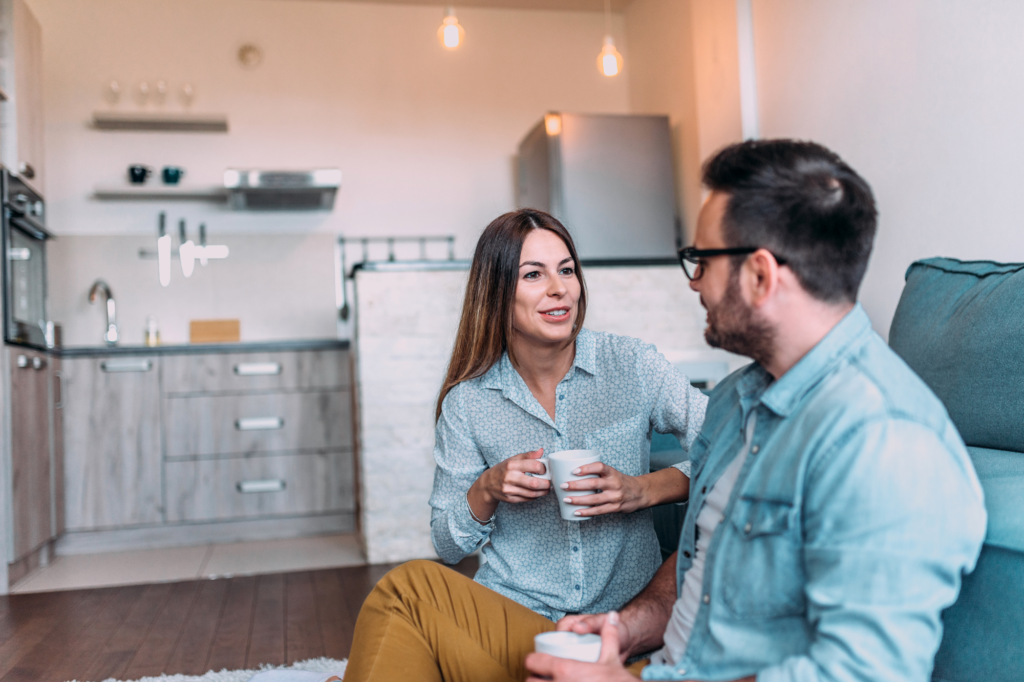 Young couple sitting on the floor at home, enjoying coffee and having a relaxed conversation in a modern kitchen about hearing God's voice.